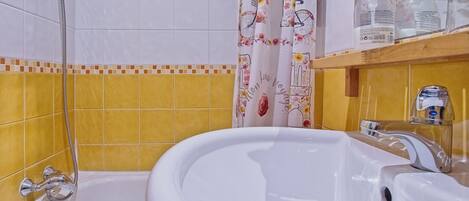 Un baño con bañera, ducha y un estante con artículos de aseo.