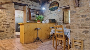 Un interior rústico de piedra con una barra de madera, suelo de baldosas y una mesa con sillas.