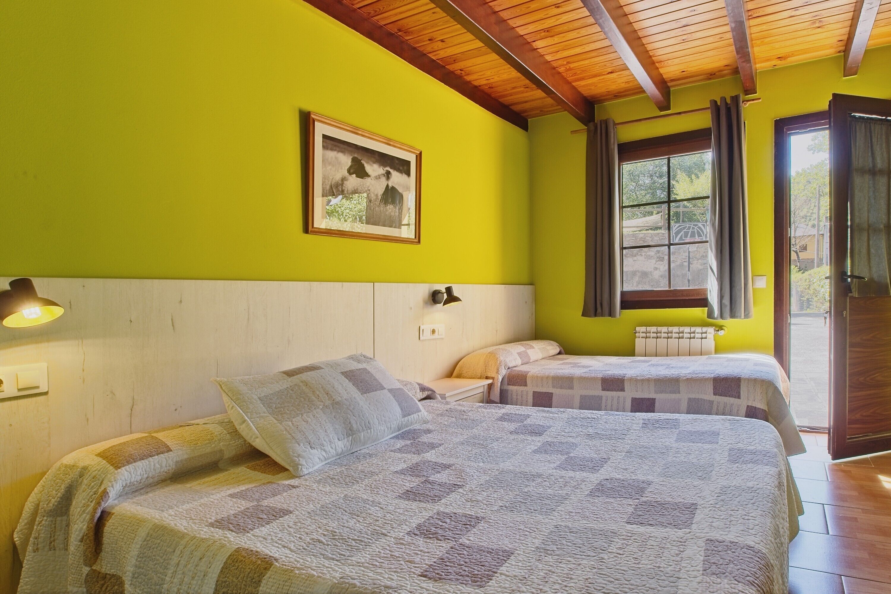 Una habitación con dos camas, techo de madera, ventana con cortinas e imagen colgada en la pared.