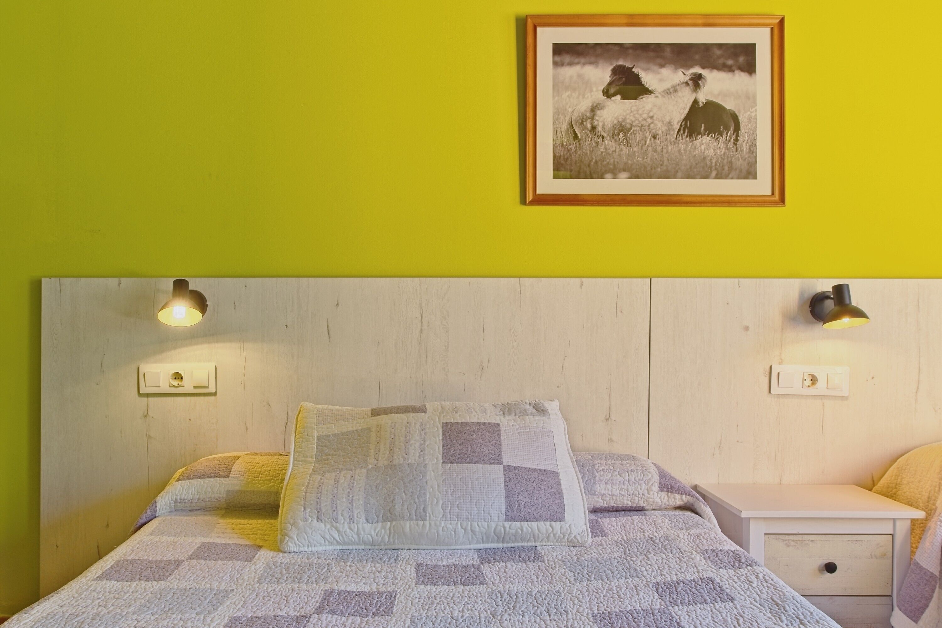 Un lit avec une couette, des lampes de chevet, une table de nuit et un tableau encadré au mur.