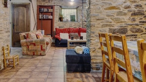 Una habitación acogedora con pared de piedra, puerta de madera, sofá rojo estampado, una mesita y una silla de madera.