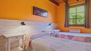 Habitación con dos camas, un aparador blanco, una mesita de noche, una ventana con cortinas y un cuadro colgado en la pared.