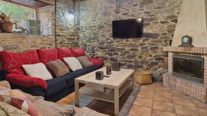 Una habitación con paredes de piedra, un sofá, una mesa, una chimenea y un televisor.