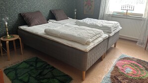 Un dormitorio con una cama, dos almohadas, una mesita de noche, una lámpara, una ventana con cortinas y una alfombra estampada.
