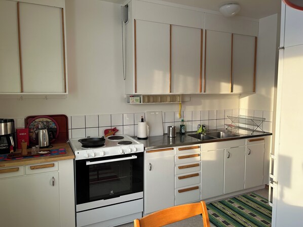 A kitchen with white cabinets, a stove, a sink, and a coffee maker.