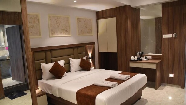 Quarto de hotel moderno com cama grande, mesa de cabeceira, guarda-roupa embutido e casa de banho visível através de uma porta aberta.