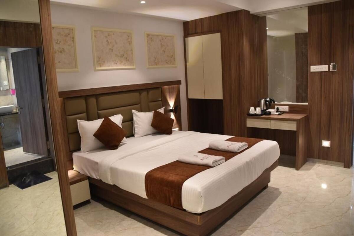 A modern hotel room with a large bed, a bedside table, a built-in wardrobe, and a bathroom visible through an open door.