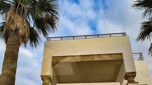 A building with a large black gate, white textured walls, and a balcony with a railing. - DAR EL NOUR | Villa pied dans l'eau | 130 m² | Rooftop avec vue exceptionnelle (Korba)