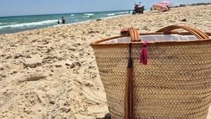 A beach scene with a woven basket in the foreground, a red scooter, and a pink umbrella in the background. - DAR EL NOUR | Villa pied dans l'eau | 130 m² | Rooftop avec vue exceptionnelle (Korba)
