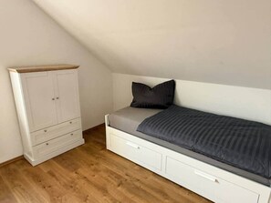 Un dormitorio con cama doble alta, un armario blanco y suelo de madera.