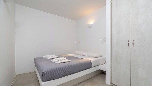 Ein schlicht eingerichtetes Schlafzimmer mit Bett, weißen Wänden und einem Kleiderschrank.