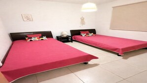 Una habitación con dos camas, cada una con una colcha roja y un cojín estampado de lunares. Entre las camas hay una mesita con una lámpara, y una decoración colgando en la pared.