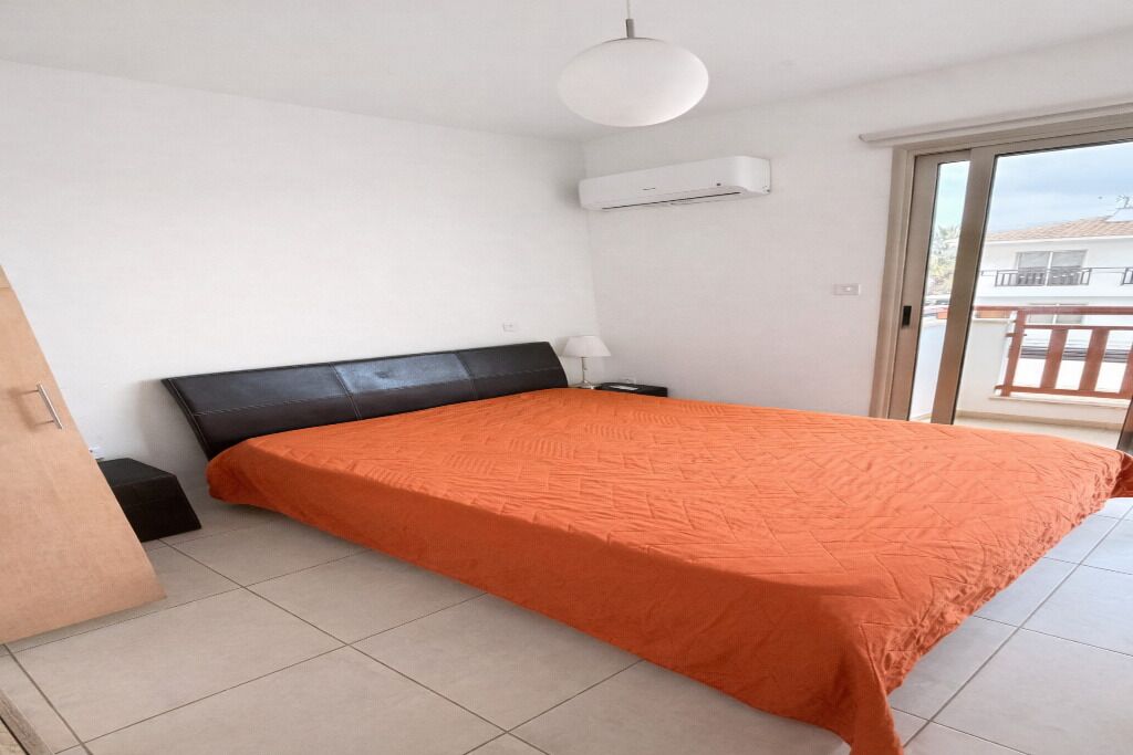 Ein Schlafzimmer mit Bett, Nachttisch, Lampe, Klimaanlage und einer Schiebetür zu einem Balkon.