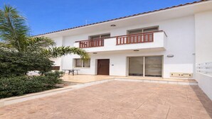 Un edificio de dos plantas con un balcón, un patio y un pequeño jardín con una palmera.