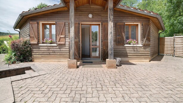 Een houten chalet met betegelde entree, houten luiken en een klein terras.