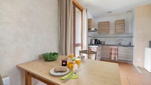 Een eethoek met een ontbijttafel, een keuken op de achtergrond en uitzicht door een open deur.