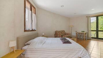 Un dormitorio con cama, una mesita, una silla, un ventanal y vistas al exterior.