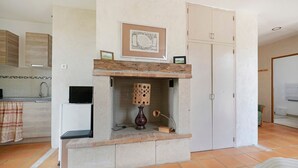 Een kamer met een open haard, een ingelijst schilderij erboven, een tafeltje met een lamp en een kledingkast.