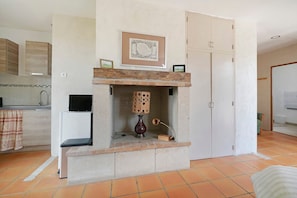 Une pièce avec une cheminée, un tableau encadré au-dessus, une petite table avec une lampe et une armoire.