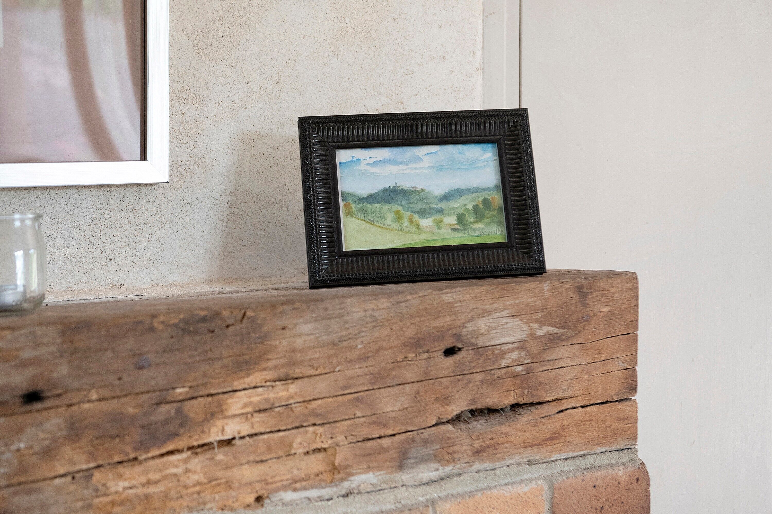 A framed picture of a landscape on a wooden shelf.