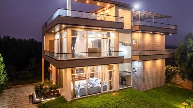 Une maison moderne à deux étages, dotée d’un balcon, de grandes fenêtres et d’un intérieur bien éclairé.