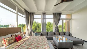 Une chambre moderne avec un grand lit, un canapé, une table basse en verre et une vue sur la verdure.