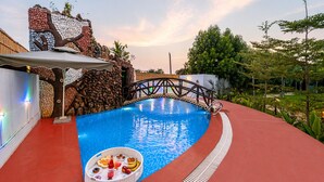 Une piscine avec un pont, entourée d’une terrasse rouge, et un mur décoratif orné d’un motif d’arbre.