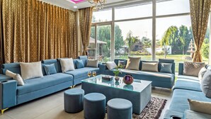 Un salon moderne avec un canapé bleu, une table basse en verre et une vue sur un jardin.