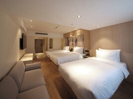 A hotel room with two beds, a sofa, a TV, and a painting on the wall.