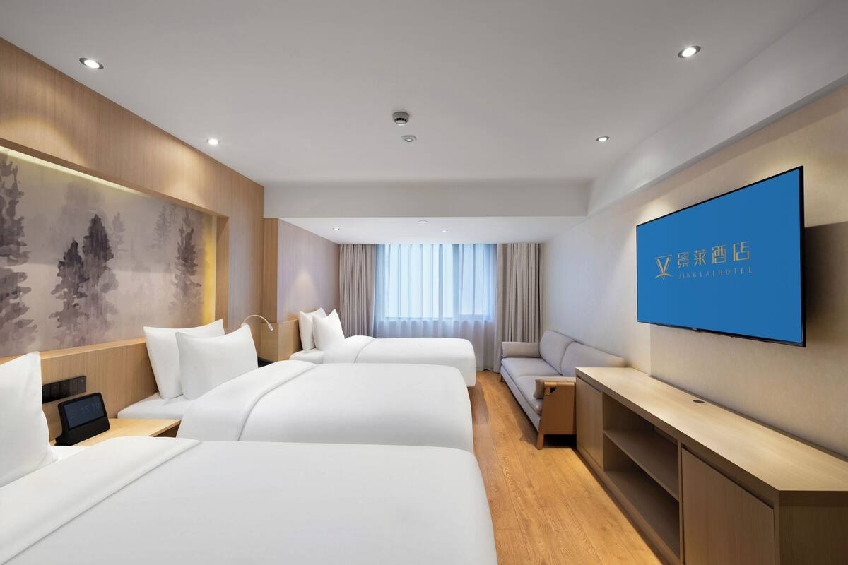 A hotel room with two beds, a TV, a desk, and a large window with curtains.