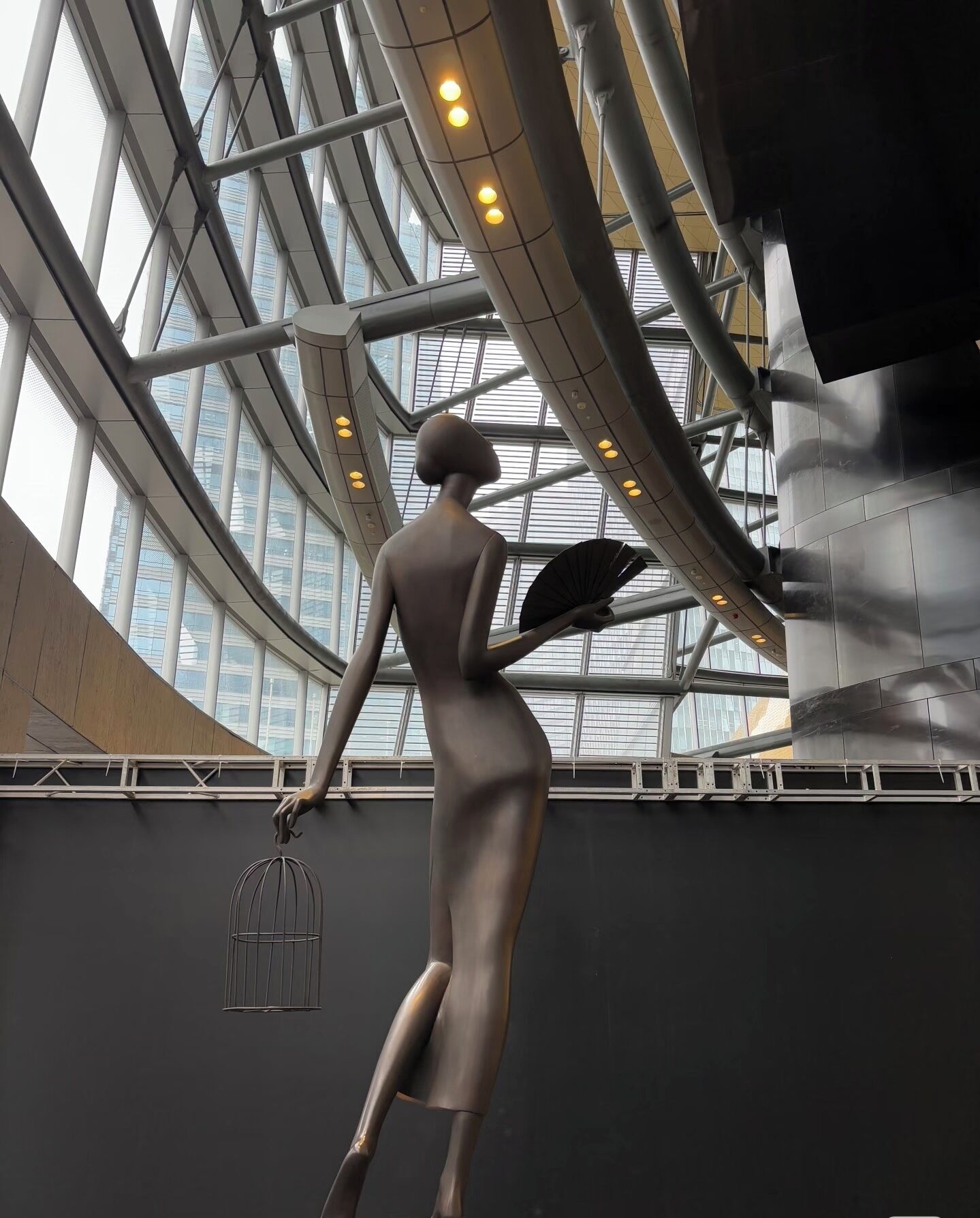 A modern interior with a large glass ceiling, metal beams, and a sculpture of a human figure.