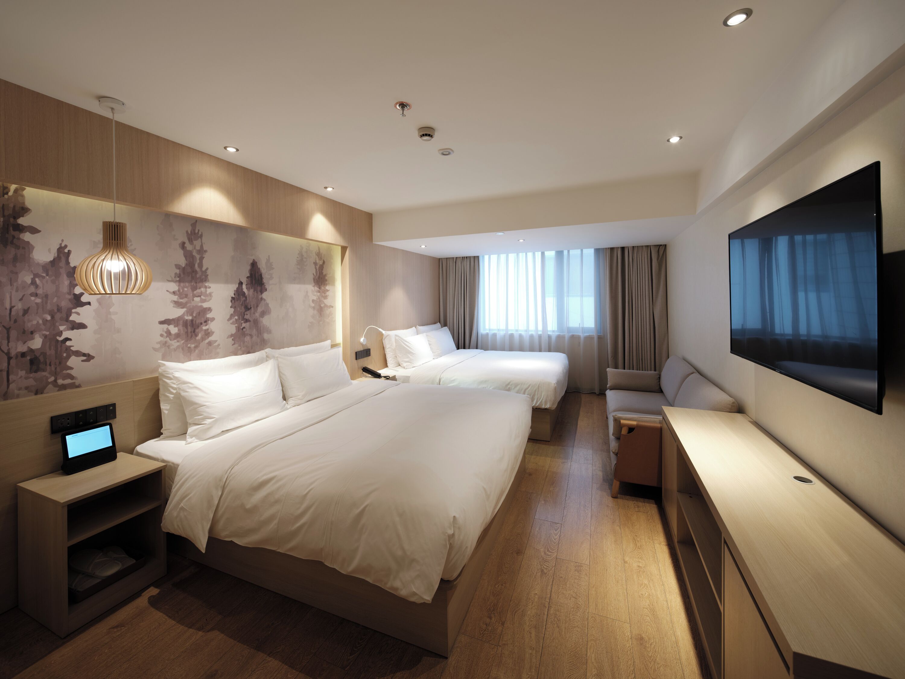 A hotel room with two beds, a TV, a desk, and a large window with curtains.