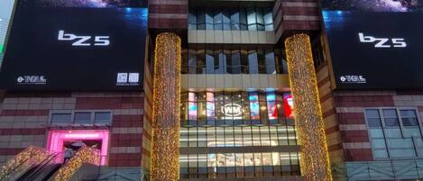 A multi-story building with large digital billboards, a prominent entrance with illuminated signage, and a surrounding area with a covered walkway.