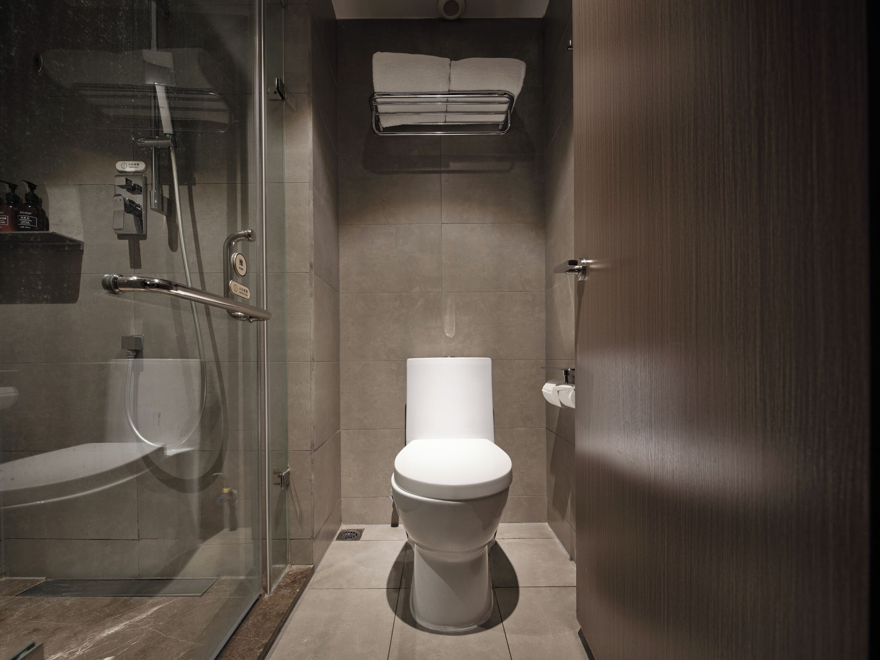 A modern bathroom with a glass-enclosed shower, a toilet, and a towel rack.