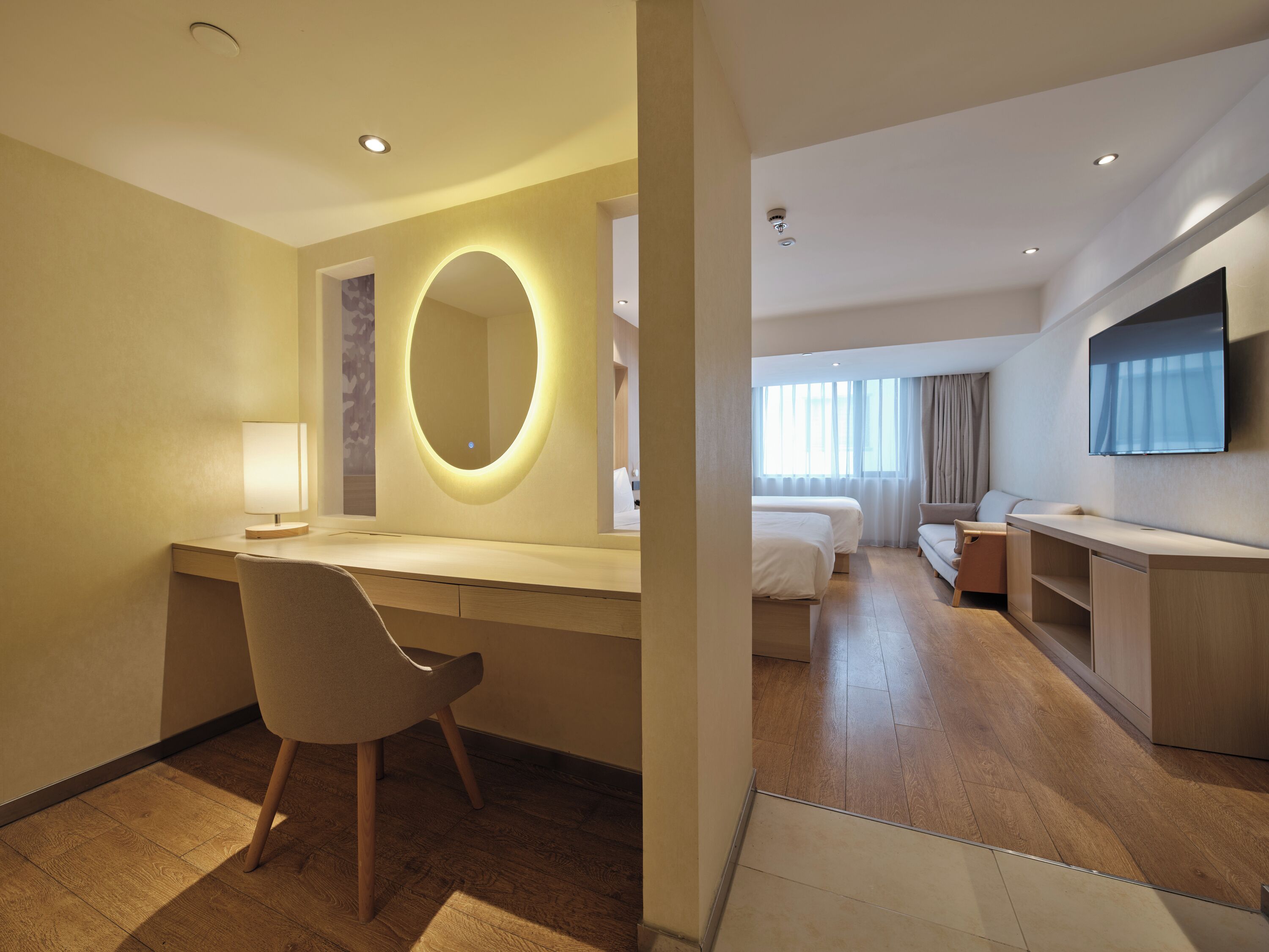 Une chambre d’hôtel équipée d’un bureau, d’une chaise, d’un lit, d’une télévision et d’un grand miroir.
