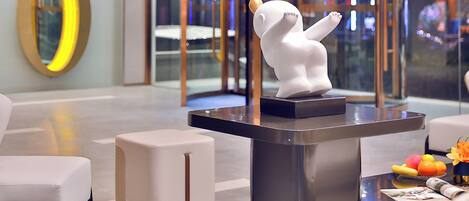 A modern lobby with a white bear statue on a black pedestal, a round mirror, and a seating area with a fruit bowl.
