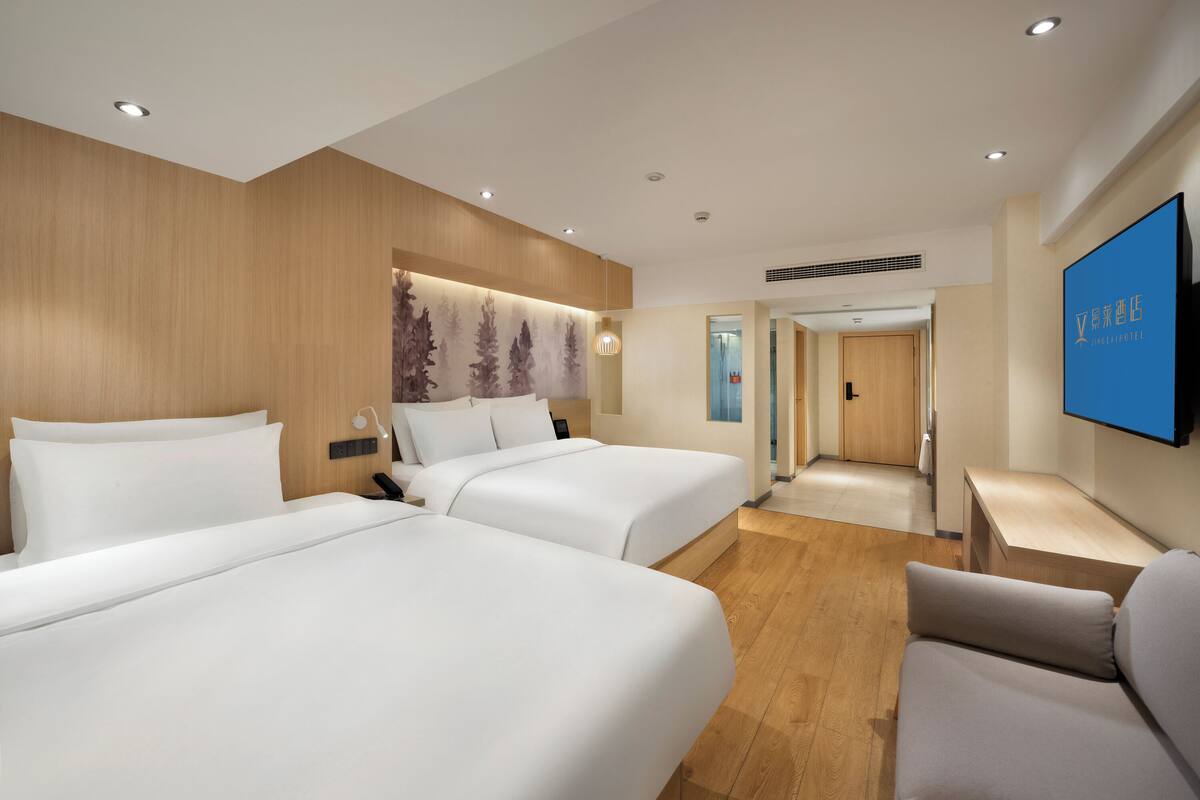 A hotel room with two beds, a flat-screen TV, a desk, and a sofa.