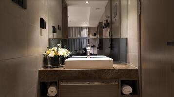 Un baño moderno con un espejo grande, un lavamanos de mármol y un florero con flores.