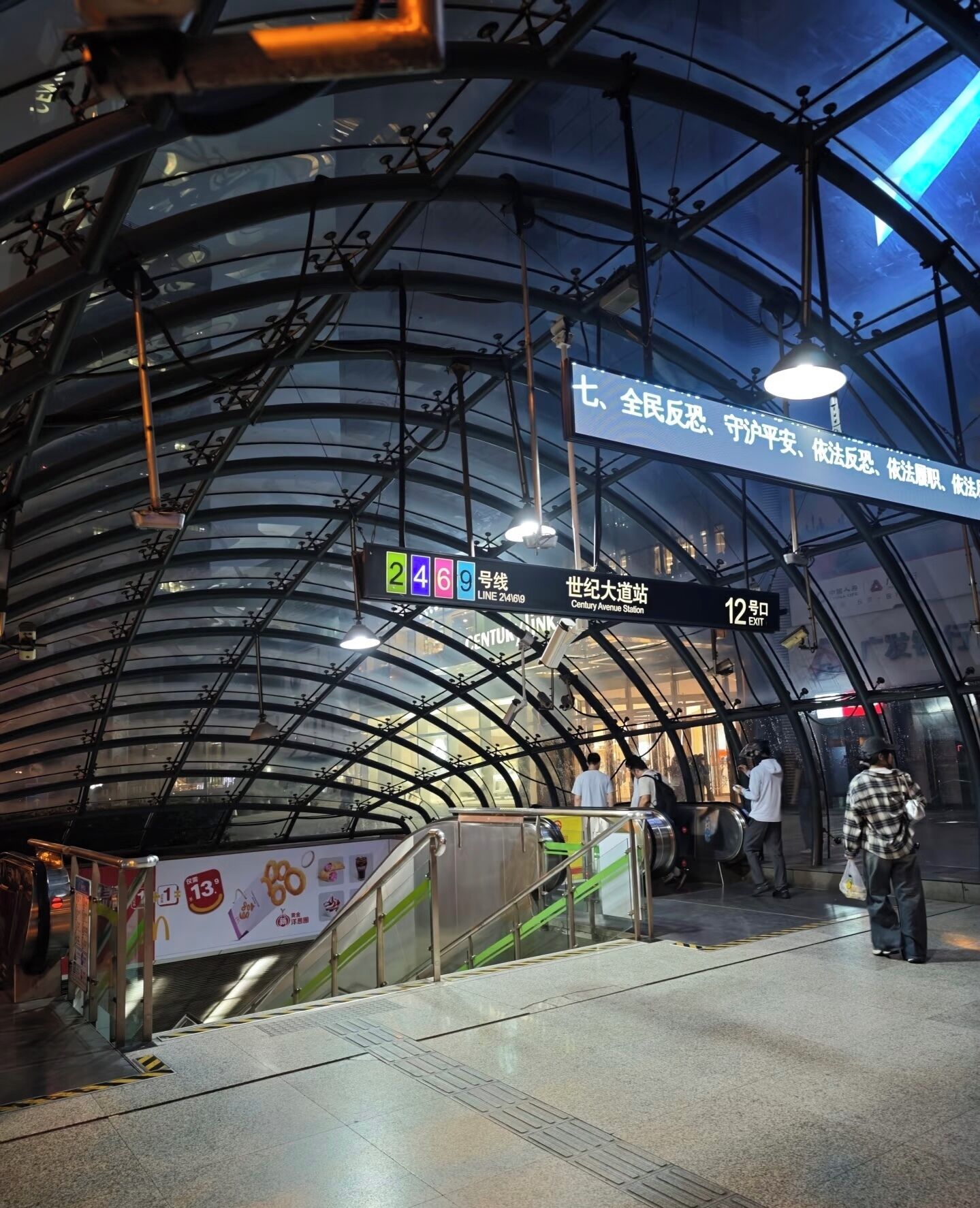 A subway station with a curved glass ceiling, signage indicating exit 12, and a digital display for Line 24.