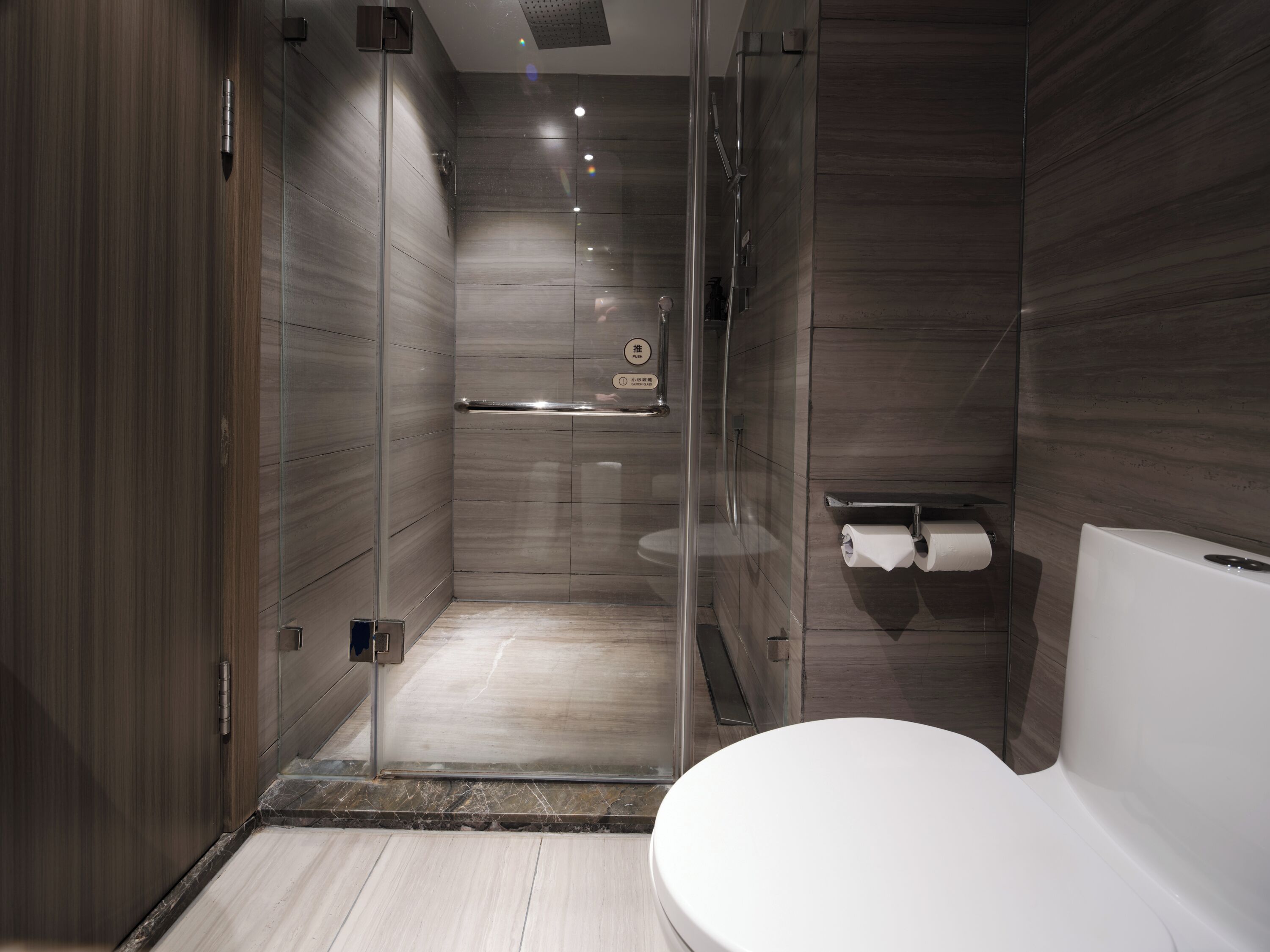 Een moderne badkamer met een douchecabine van glas, een toilet en een handdoekhouder.
