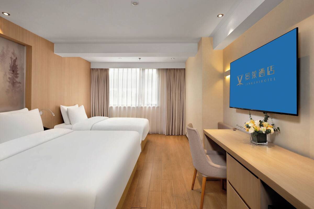 A hotel room with two beds, a desk, a chair, a TV, and a window with curtains.