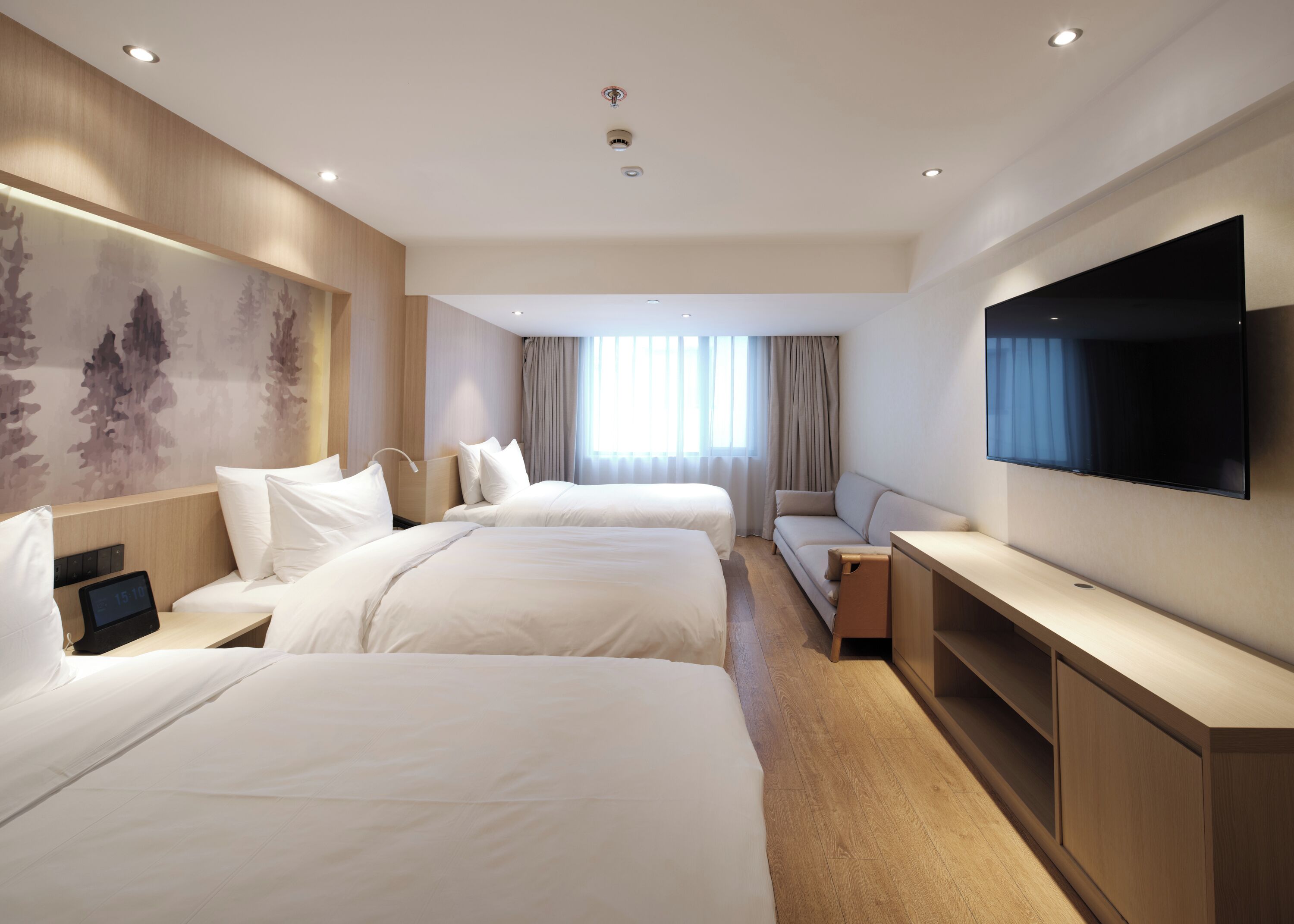 Een hotelkamer met drie bedden, een flatscreen televisie, een bureau en een groot raam met gordijnen.