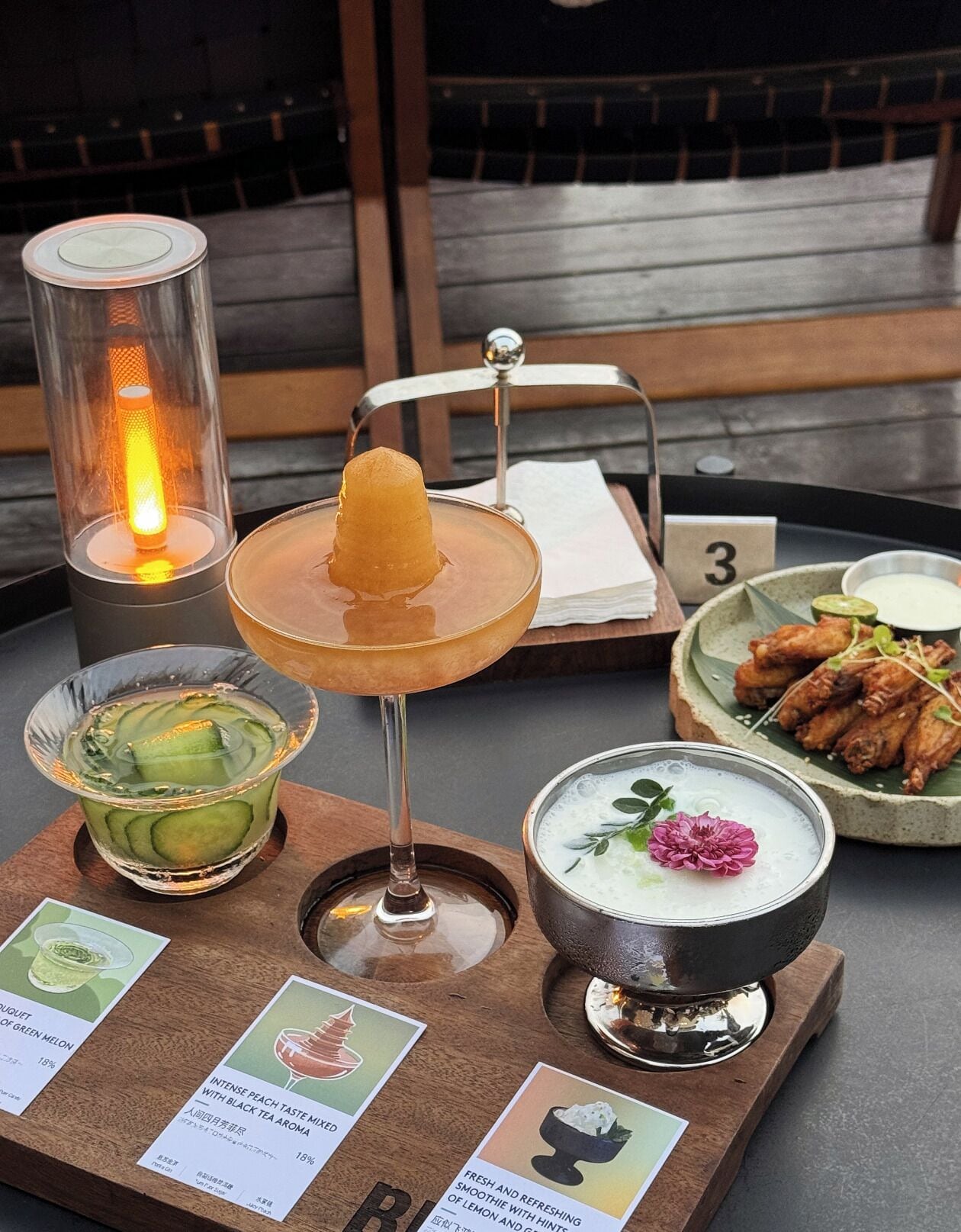 A table with a variety of beverages and dishes, including a cocktail with a fruit garnish, a bowl of soup with a flower, and a plate of fried chicken wings.