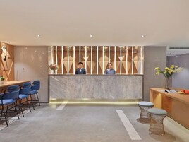 Un área de recepción moderna con un mostrador de mármol, sillas azules y un separador de madera con listones verticales.