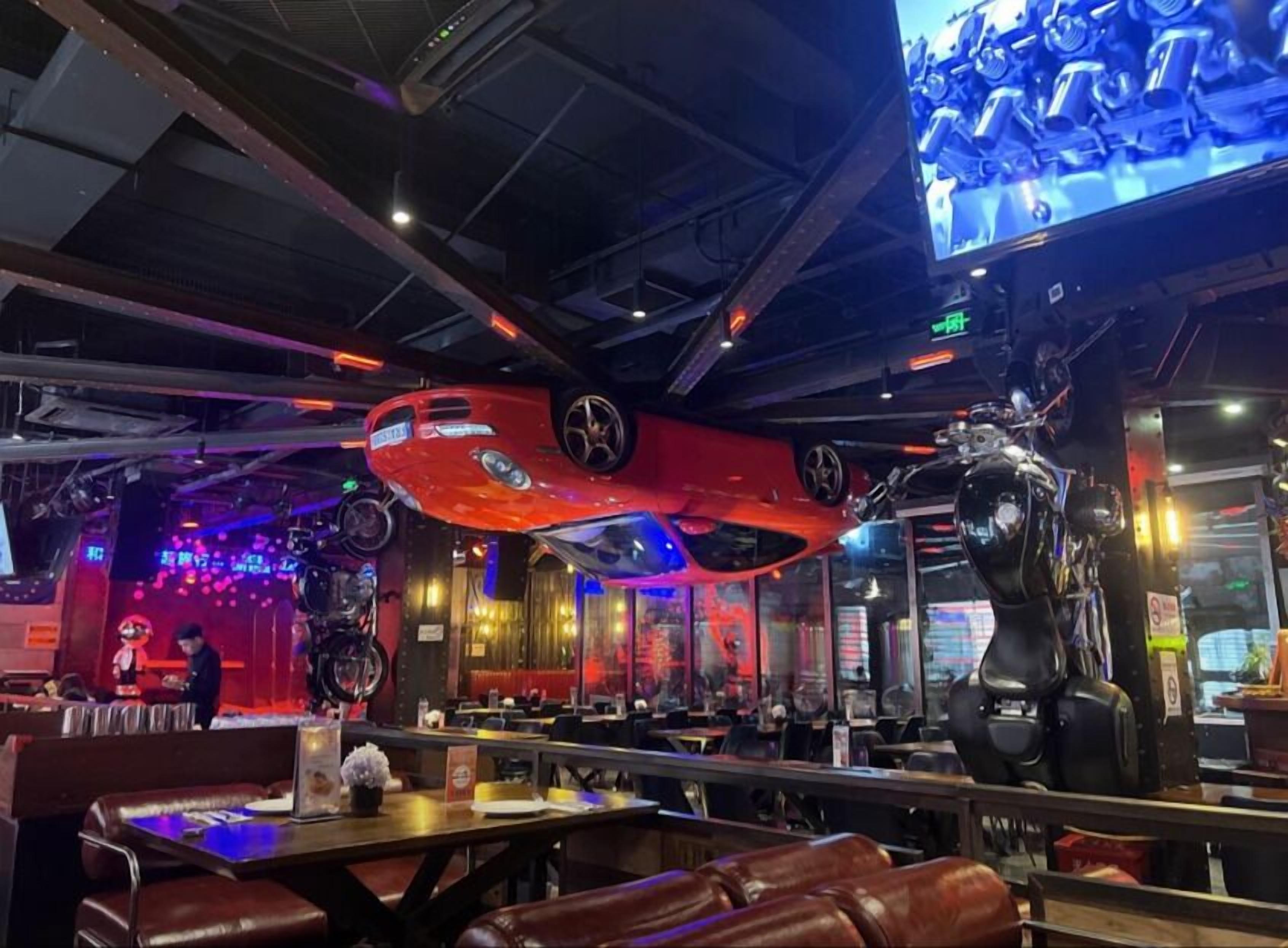 A restaurant interior with high ceilings, exposed beams, and a large screen displaying a sports event.