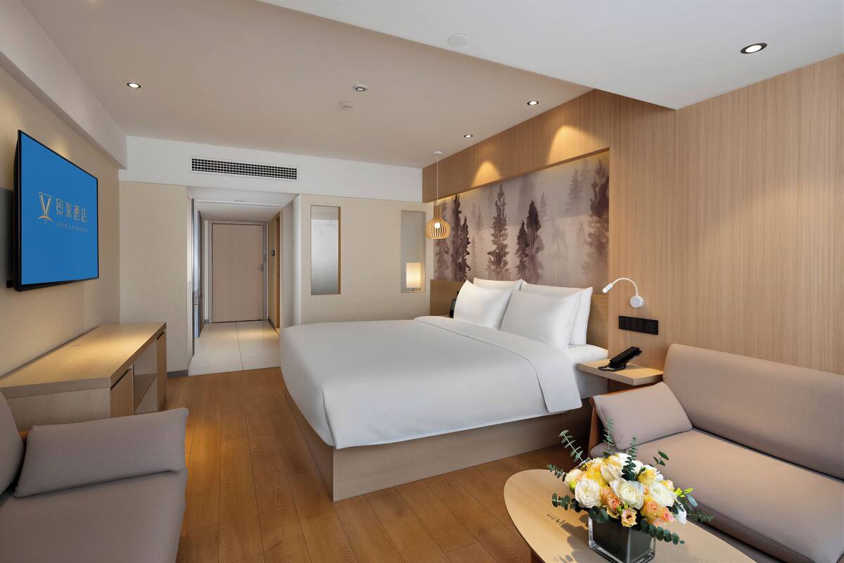 A modern hotel room with a large bed, a sofa, a desk, and a wall-mounted TV.