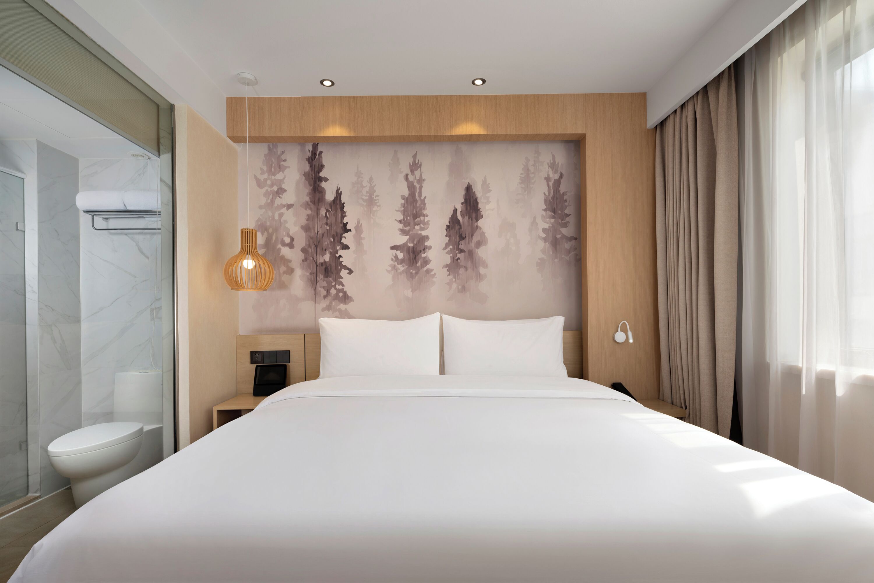 Habitación de hotel con una cama grande, una mesita de noche, una lámpara de pared y zona de ducha.