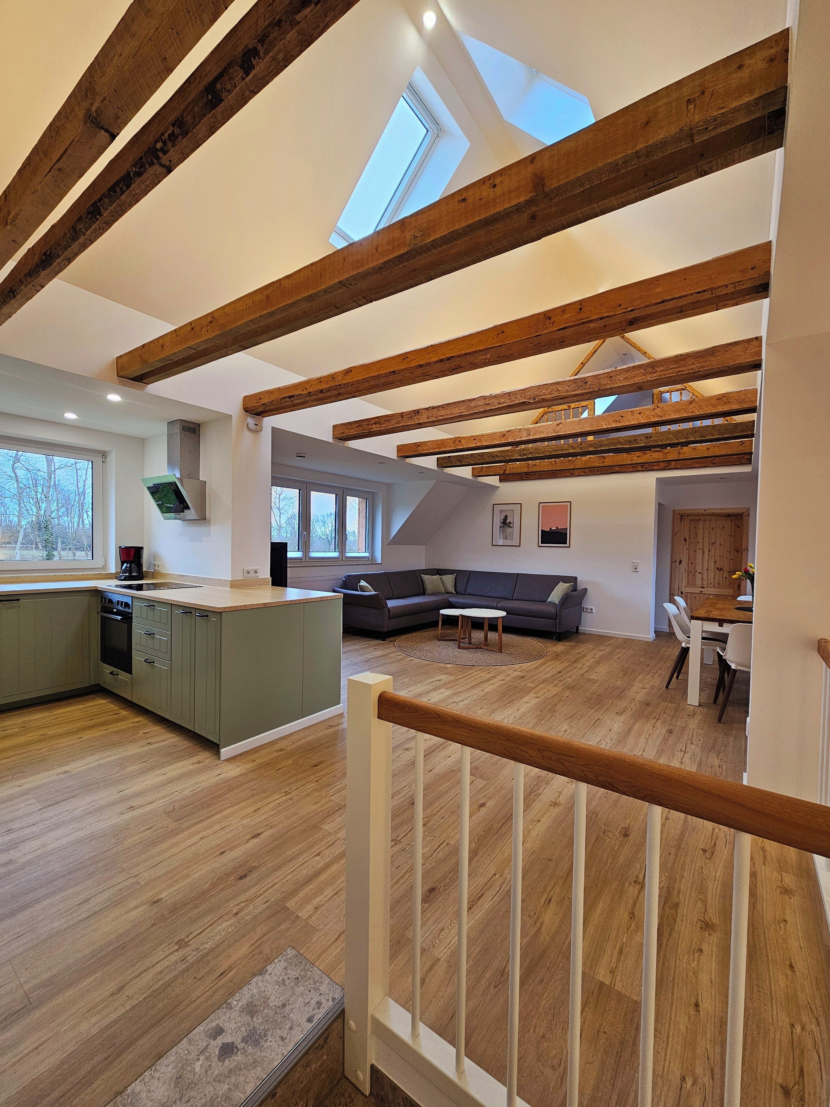 A spacious loft with exposed wooden beams, a kitchen with a built-in island, a dining area, and a living room with a sofa and coffee table.