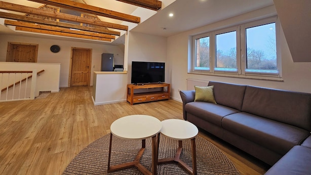 A modern living room with exposed wooden beams, a sofa, a TV, and a dining area.