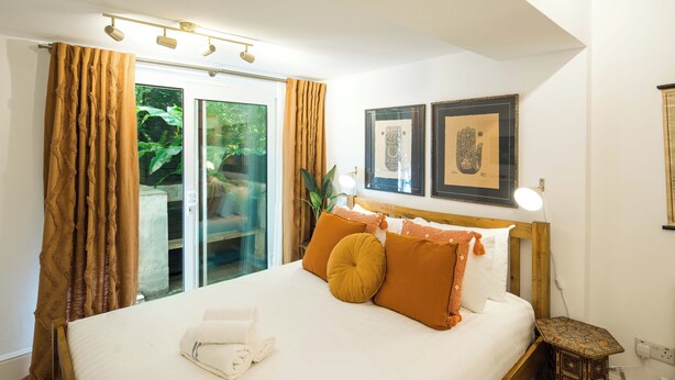 Een slaapkamer met een groot bed, een nachtkastje met een lamp en uitzicht op groen door de glazen deur.